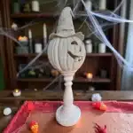 Örümcek ağları ve loş ışıklarla dekore edilmiş bir ortamda, kırmızı runner üzerinde duran cadı şapkalı ham polyester kabak heykeli. Ürünün iç mekana entegre edilmiş Halloween atmosferi.