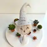 Beyaz bir platform üzerinde sukulentlerle çevrili, cadı şapkalı ham polyester kabak heykeli (POL78). Boyanabilir Halloween dekoratif figür.